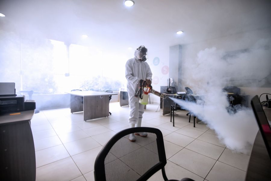 Technician in protective suit electrostatic disinfecting an office with fogging spray