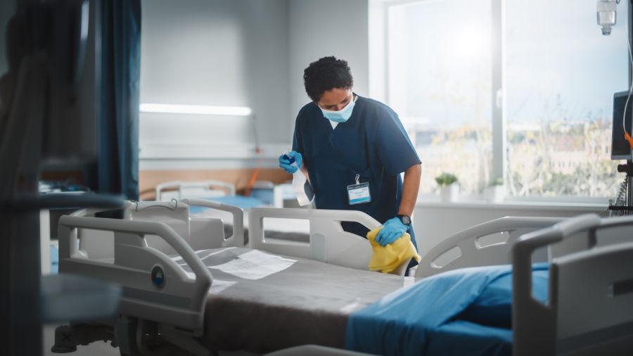 Hospital cleaner disinfecting a patient bed in a medical facility room